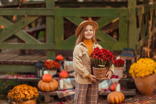 Fille au chapeau avec un décor d'automne avec des citrouilles et des fleurs