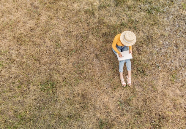 Une fille au chapeau dessine un croquis dans la nature - une vue d'en haut