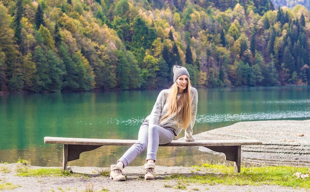 Photo une fille au chapeau est assise sur un banc dans le contexte d'une forêt d'automne et d'un lac