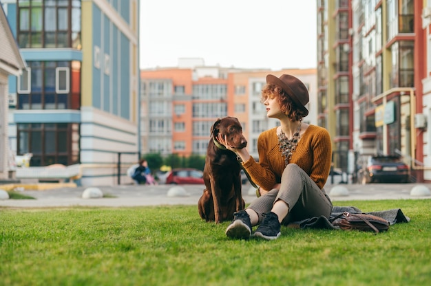 Fille au chapeau est assise avec un beau chien brun sur la pelouse