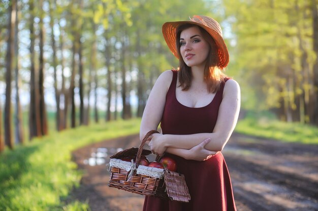 Une fille au chapeau lors d'une promenade dans le parc. Une fille avec un panier marche au printemps. La fille marche le long de la route au coucher du soleil.