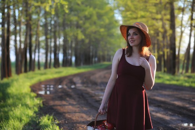 Une fille au chapeau lors d'une promenade dans le parc. Une fille avec un panier marche au printemps. La fille marche le long de la route au coucher du soleil.