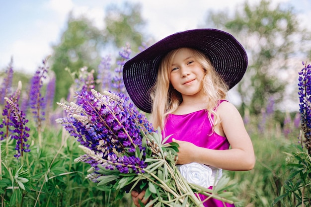 La fille au chapeau marche dans un champ de lupins.