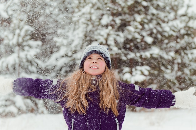 Fille au chapeau de neige jetant de la neige à l'extérieur des arbres d'hiver