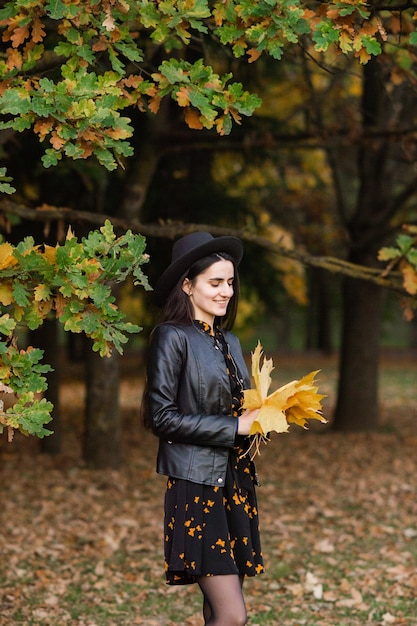 Une fille au chapeau noir tient des feuilles d'automne jaunes dans ses mains