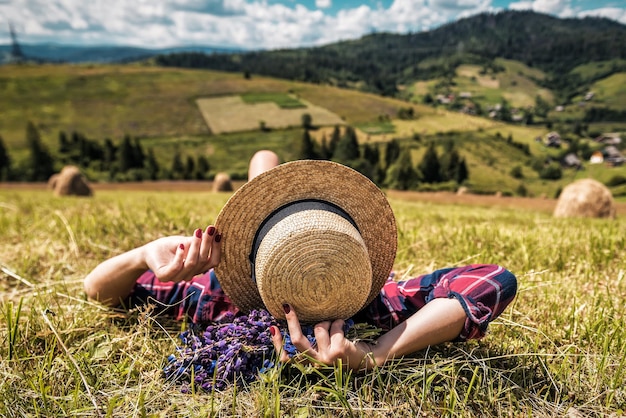 Fille au chapeau de paille allongé sur l'herbe dans les montagnes