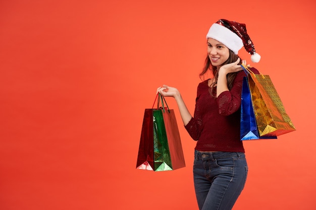 Fille au chapeau de père Noël souriant avec des sacs de Noël sur fond orange