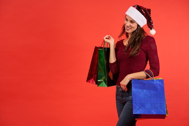 Photo fille au chapeau de père noël souriant avec des sacs de noël sur fond orange