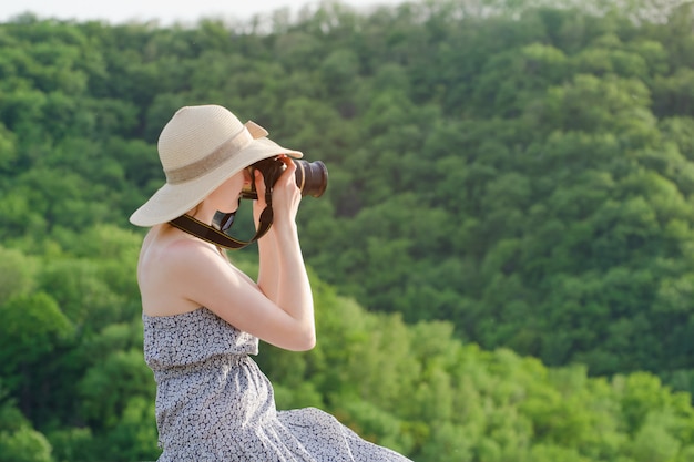 Fille au chapeau prend des photos dans le contexte de la forêt verte