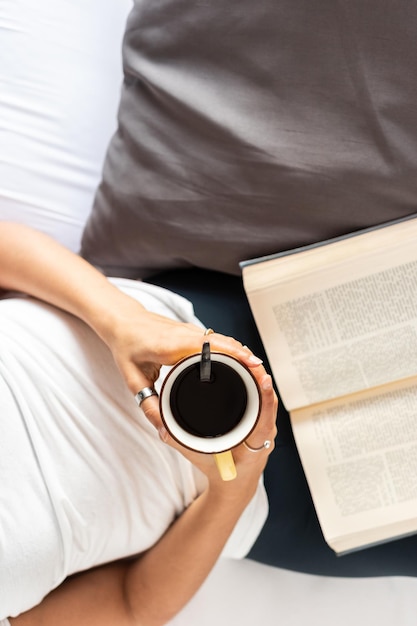 Fille au lit avec une tasse de café dans les mains et un livre