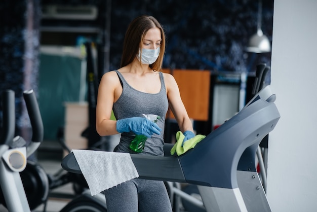 La fille au masque désinfectant le matériel de gym pendant une pandémie.