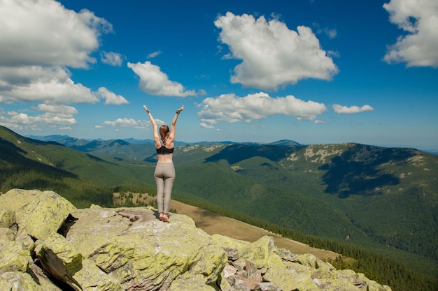 La fille au sommet de la montagne leva les mains vers le haut Large vue sur la montagne d'été au lever du soleil et la chaîne de montagnes lointaine couverte Concept de beauté de la nature