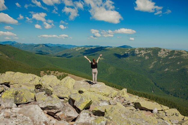 La fille au sommet de la montagne leva les mains vers le haut Large vue sur la montagne d'été au lever du soleil et la chaîne de montagnes lointaine couverte Concept de beauté de la nature