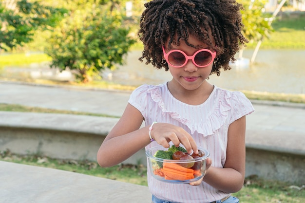 Fille aux cheveux afro, manger des légumes à l'extérieur