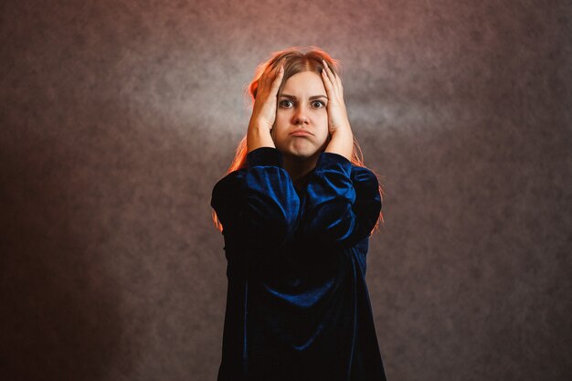 Fille aux cheveux blonds posant émotionnellement sur un fond gris. Ses cheveux sont allumés en rouge