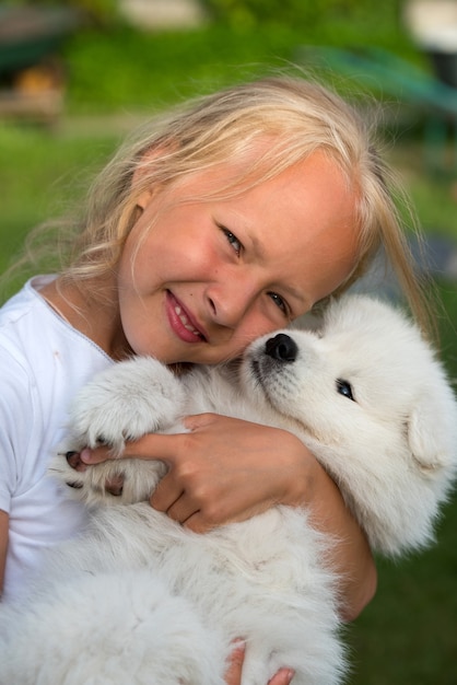 Fille aux cheveux blonds tient dans les mains un petit chiot blanc Samoyède