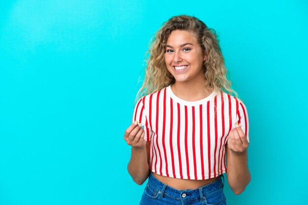 Fille aux cheveux bouclés isolé sur fond bleu faisant un geste d'argent