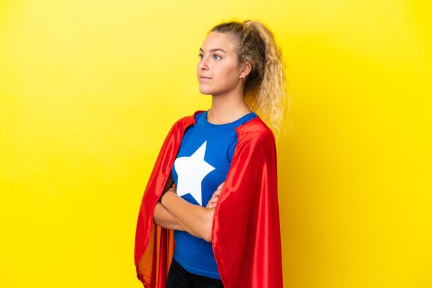 Fille aux cheveux bouclés isolé sur fond jaune en costume de super-héros avec les bras croisés