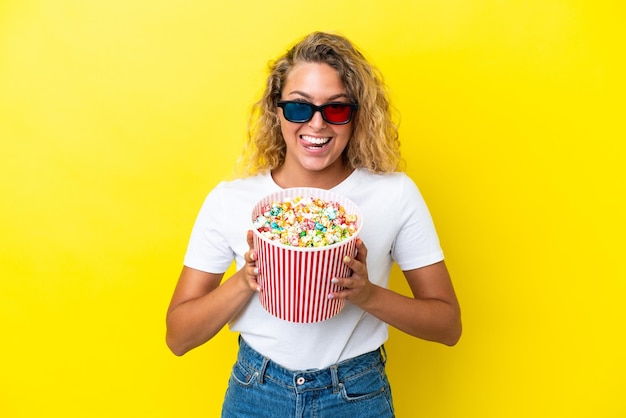 Fille aux cheveux bouclés isolé sur fond jaune avec des lunettes 3d et tenant un grand seau de pop-corn