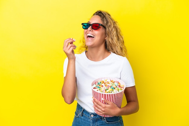 Fille aux cheveux bouclés isolée sur fond jaune avec des lunettes 3d et tenant un grand seau de pop-corn