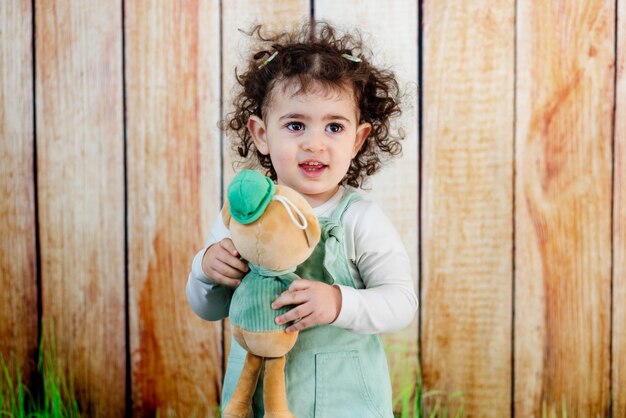 Une fille aux cheveux bouclés les mains enroulées autour d'un ami en peluche montrant un lien d'amour en studio