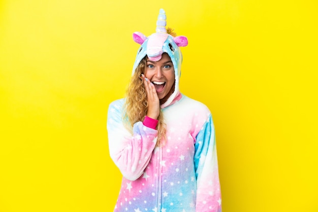 Fille aux cheveux bouclés portant un pyjama licorne isolé sur fond jaune avec une expression faciale surprise et choquée