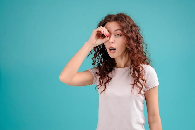 Fille aux cheveux bouclés, regardant à travers sa main isolée sur fond turquoise