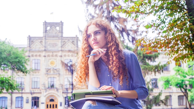 Fille aux cheveux bouclés rousse caucasienne assise près de son université