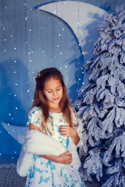 Une fille aux cheveux bruns à côté de l'arbre de Noël