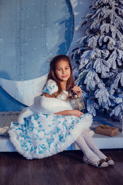 Une fille aux cheveux bruns à côté de l'arbre de Noël