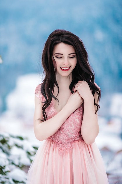 Fille aux cheveux châtains, aux yeux bleus et une robe rose sur le fond des montagnes d'hiver