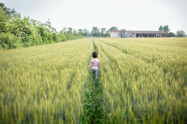 Une fille aux cheveux courts et au haut rose s'éloigne dans un champ de blé vert.