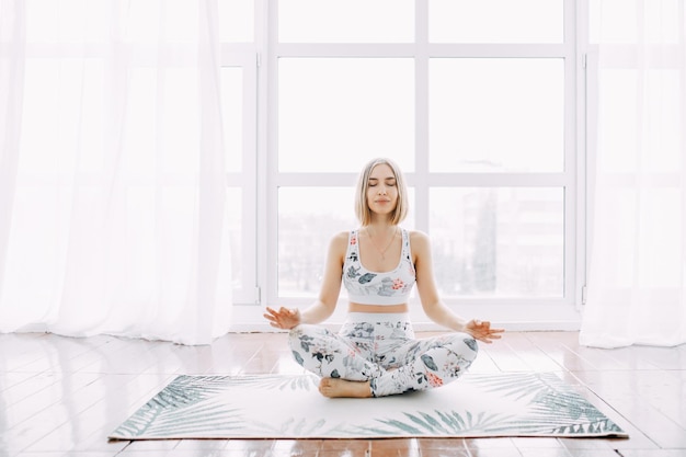 La fille aux cheveux courts fait des exercices physiques des exercices de yoga et s'étire sur un tapis contre à la maison