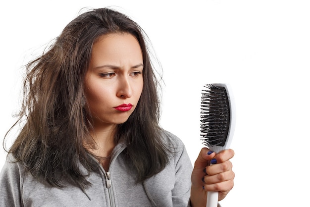 Une fille aux cheveux hirsutes ébouriffés tient un peigne dans ses mains. problèmes de cheveux, de cuir chevelu et de pellicules isolés sur blanc