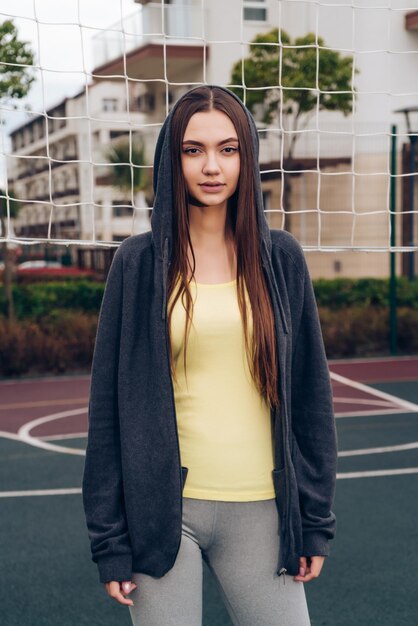 Fille aux cheveux longs confiante posant sur le terrain de sport en regardant la caméra menant une vie active