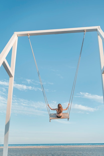 Fille aux cheveux longs sur une corde se balancer contre sur la mer et le ciel bleu fond Concept de liberté et de négligence enfant cadre vertical