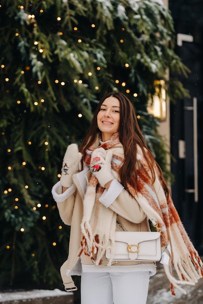 Une fille aux cheveux longs dans une écharpe et avec un sac à main blanc marche dans la rue en hiver