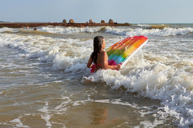 Photo une fille aux cheveux longs entre dans une vague de la mer avec un matelas gonflable multicolore