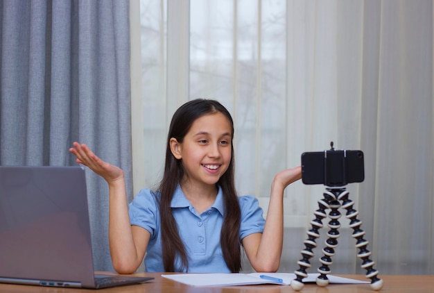 Une fille aux cheveux longs foncés vêtue d'un T-shirt bleu sourit communique des blogs prend des photos d'elle-même au téléphone formation en ligne de communication en ligne