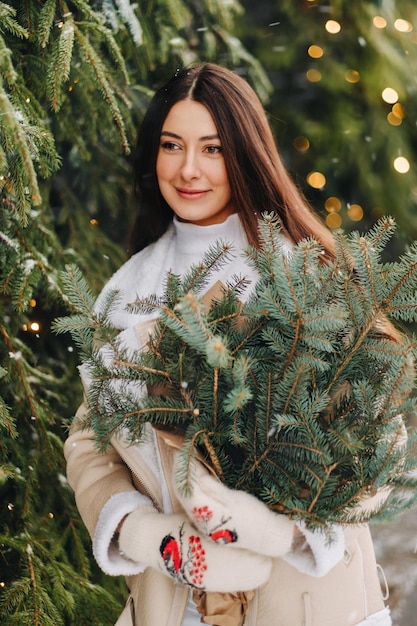 Une fille aux cheveux longs en hiver dans la rue avec un bouquet de branches de sapin frais