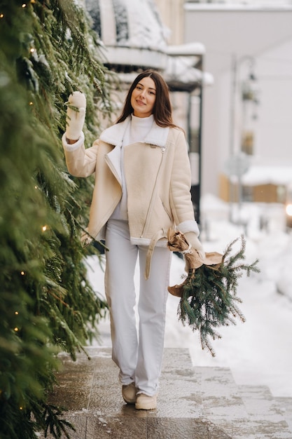 Une fille aux cheveux longs en hiver dans la rue avec un bouquet de branches de sapin frais