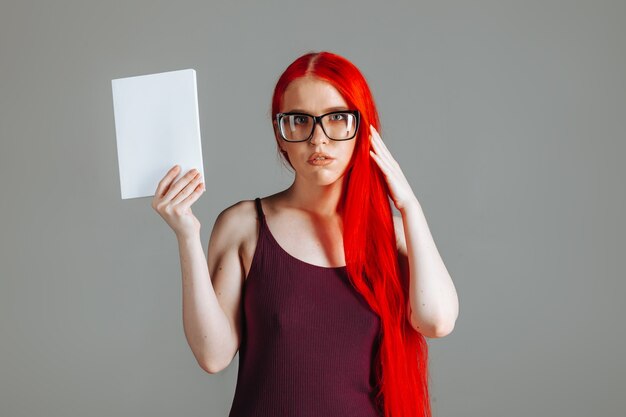 Fille aux cheveux longs rouges portant des lunettes avec un livre blanc