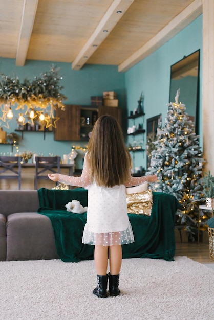 Une fille aux cheveux longs tourne le dos au salon décoré pour Noël