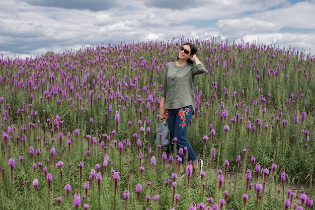 Une fille aux cheveux noirs se promène dans un champ de fleurs par temps clair d'été