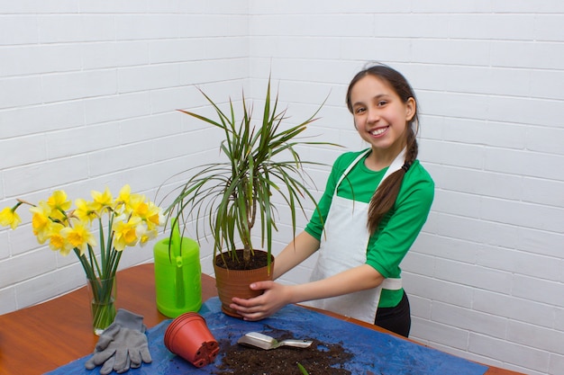 Fille aux cheveux noirs un tablier fait de la floriculture à la maison tenant un pot de fleurs dans ses mains