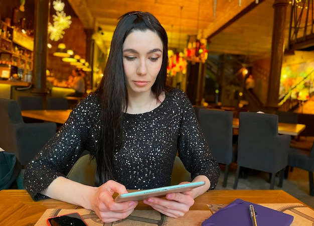 Une fille aux cheveux noirs travaille dans un café avec une tablette, un téléphone et un ordinateur portable à proximité. Coworking, organisation du workflow. Concept d'entreprise.