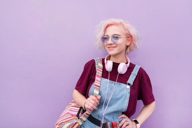 Fille aux cheveux roses debout dans le contexte d'un mur violet à la recherche dans l'appareil photo