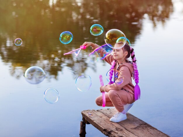 une fille aux cheveux roses un soir d'été lors d'une promenade laisse des bulles de savon sur l'eau