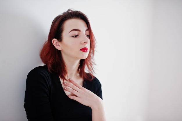 Fille aux cheveux rouge sur la tunique de robe noire contre le mur blanc à la salle vide.