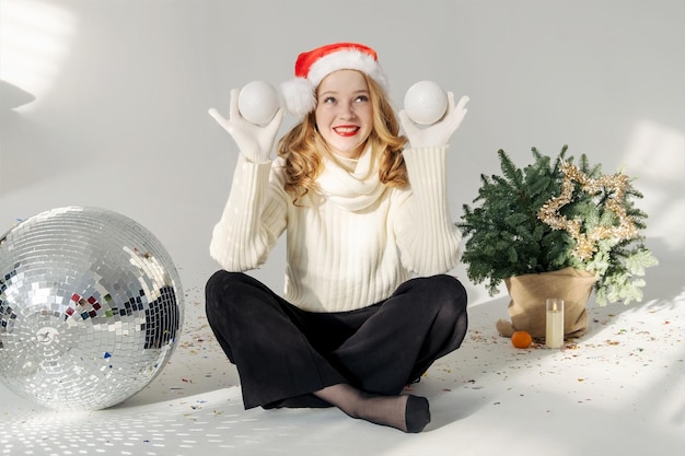 Fille aux cheveux rouges et bonnet de Noel tient une boule de jouet de neige de Noël dans sa main. Elle sourit